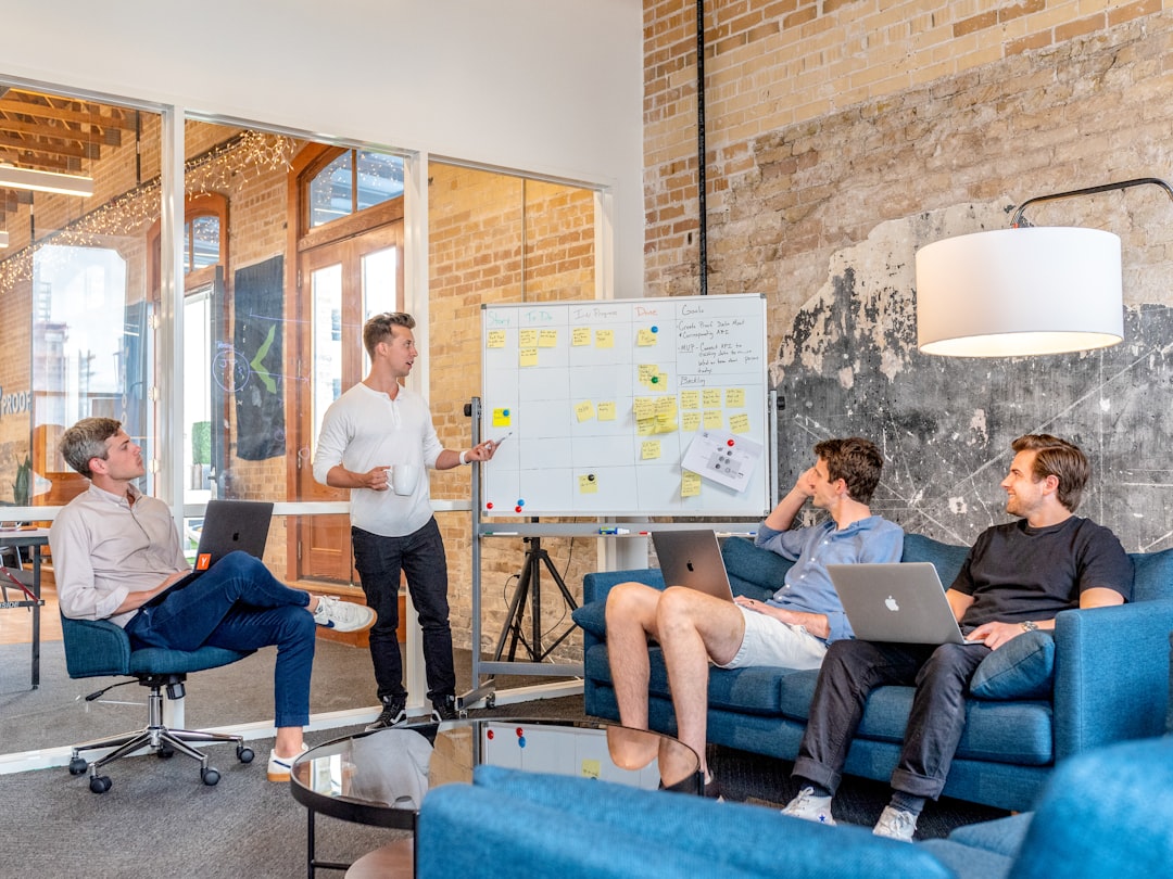 ai seo agency — three men sitting while using laptops and watching man beside whiteboard