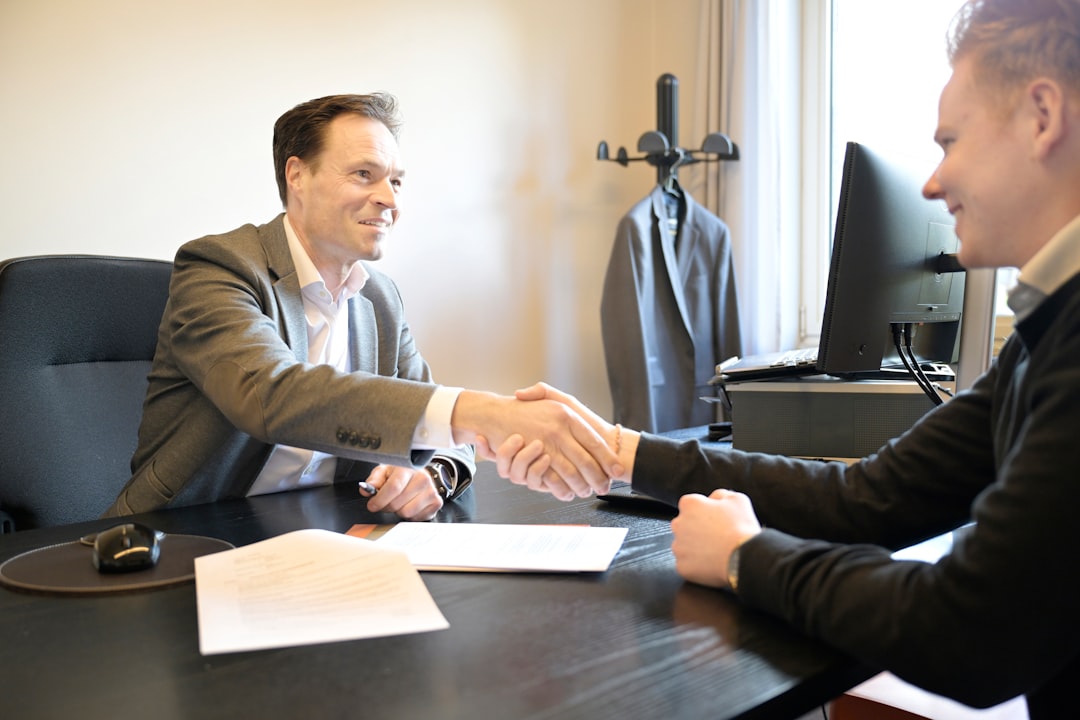 Two people shaking hands across an office desk after agreeing on a month-to-month agency deal