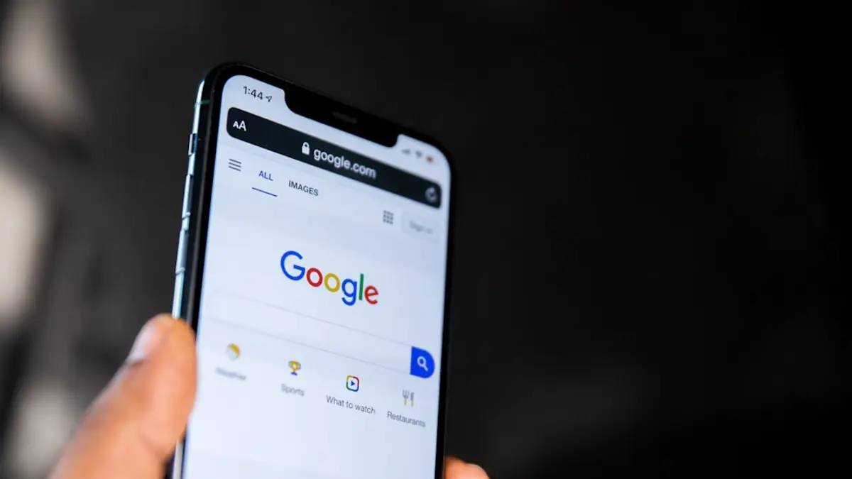 A smartphone held in one hand showing the Google search page.